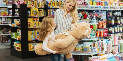 Happy mother and daughter standing at the supermarket and holding big teddy bear